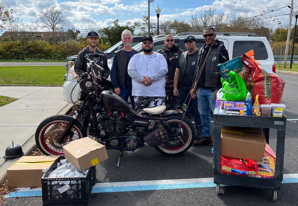 Cart and boxes of donations in from of members of Ruff Ryders Motorcycle Club and a motorcycle.  10-21-23